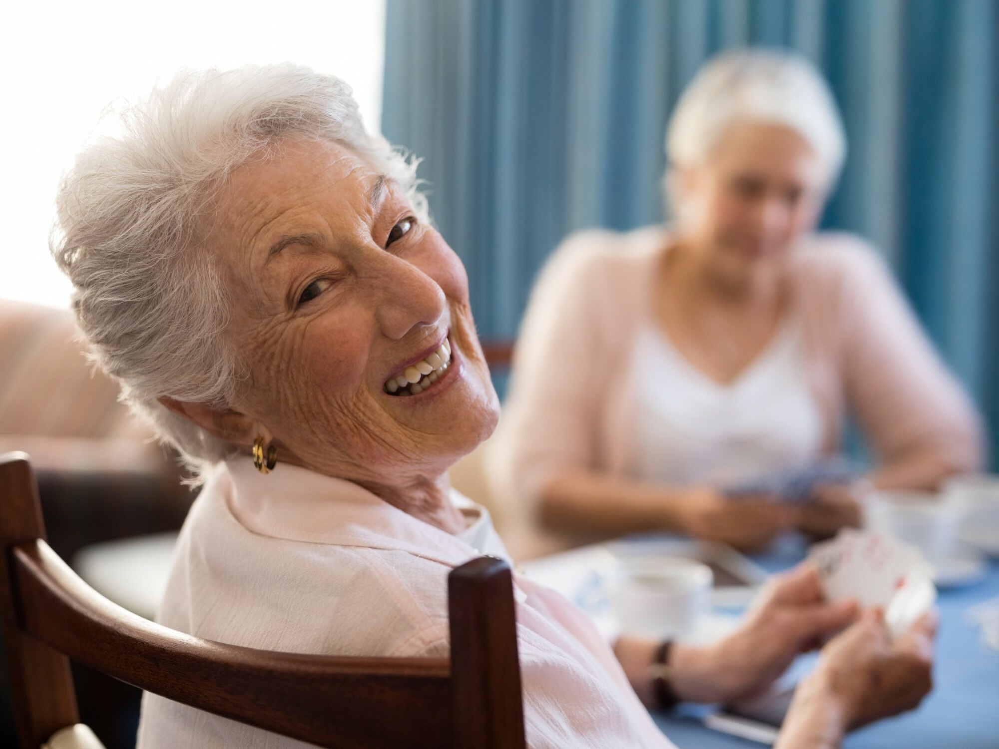 Older lady looks over her shoulder and smiles as she plays a card game with friends at home.