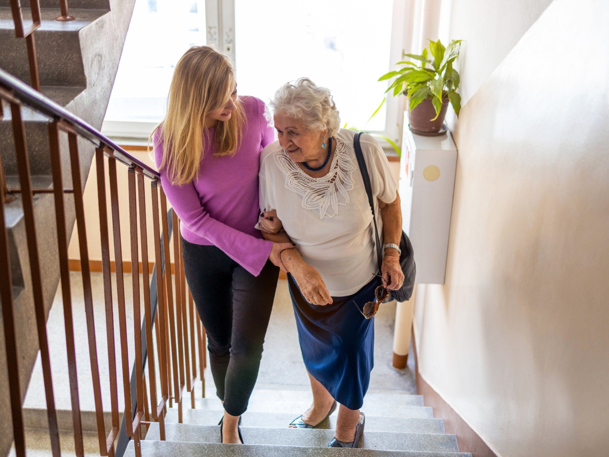 Older woman receiving assistance getting up stairs by her carer