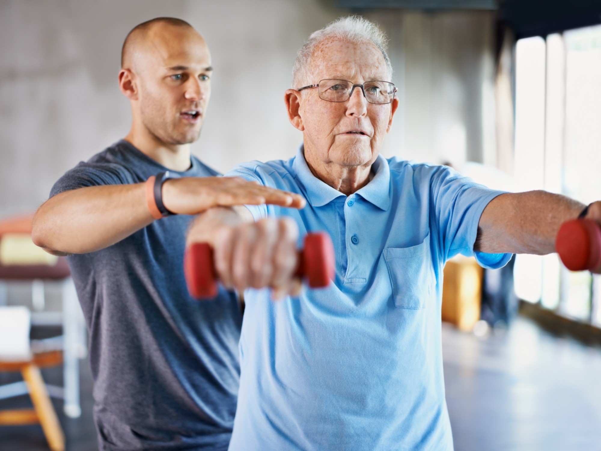 A physiotherapist is helping an older man exercise